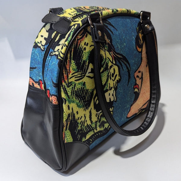 A bowler style purse with a satin body and printed image of comic book Ben Day style  art of a zombie face to face with a screaming woman. The purse has black faux leather handles, protective corners, sides, and bottom. Shown from side with handle hanging over side