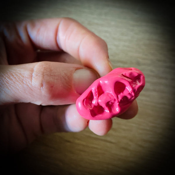 neon pink polymer clay pin in the shape of a chewed wad of gum shown held by hand for scale
