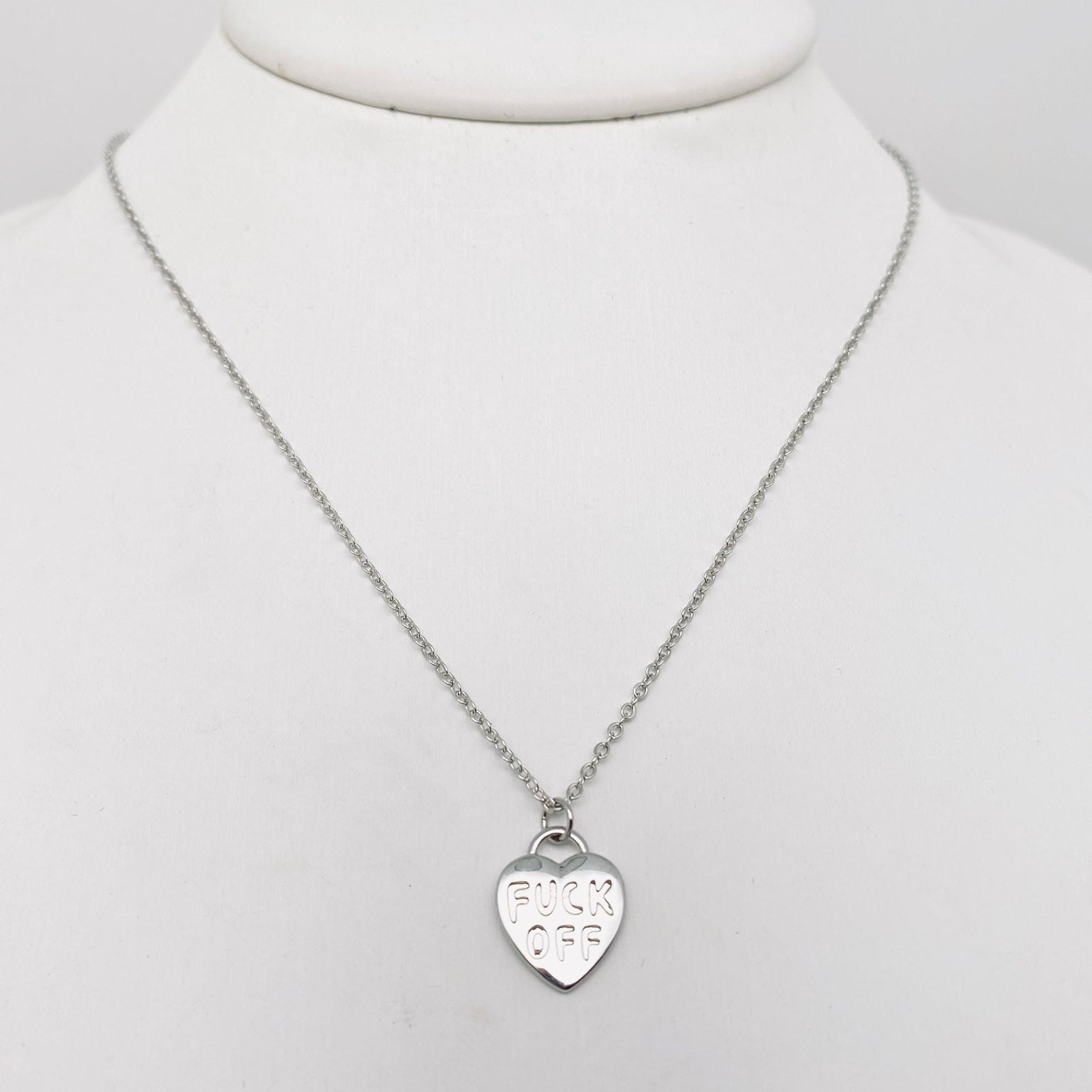 Heart-shaped pendant in silver metal engraved with “FUCK OFF” on a matching link style chain 