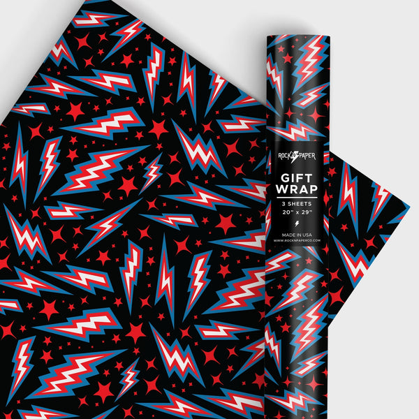 a roll of matte finish gift wrap in an all-over red, blue & white lightning bolt and red star pattern on a black background. Shown in a roll and flat