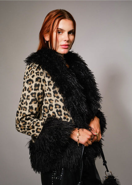 Woman wearing a leopard print coat with a black shaggy fur collar, cuffs, and bottom hem against a gray background. Shown from side