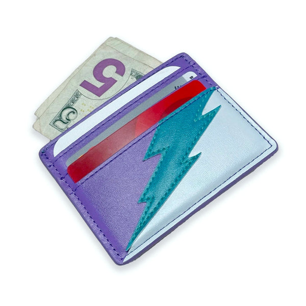 rectangular faux leather 6 slot card holder in bright purple and light blue with diagonal teal faux leather lightning bolt applique in middle. Shown from front with cards and cash