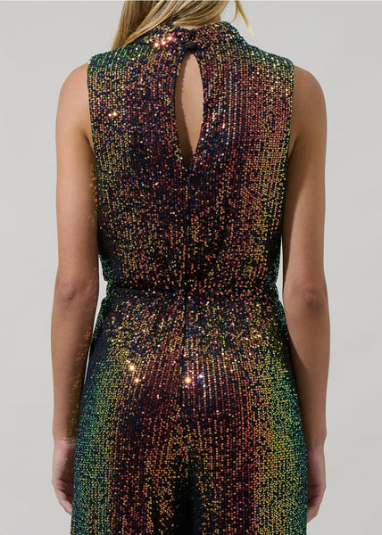 model wearing an iridescent sequin jumpsuit with shades of green, yellow, orange, and purple. Jumpsuit is sleeveless, has a mock neck, asymmetrical draped bodice detail and wide leg pants. Shown from back in closeup of back keyhole detail