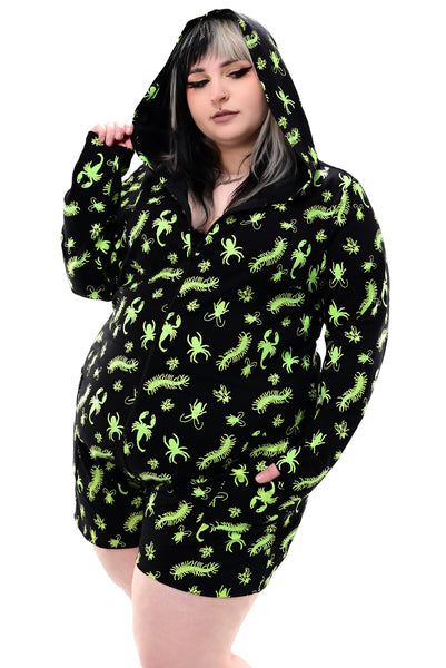 plus size model wearing a black long sleeve hooded onesie with neon green insect pattern, front zip closure, and mid-length shorts. Shown from front with hood up