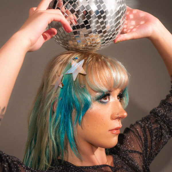 Pair of two different sized asymmetrical star-shaped acetate hair clips with iridescent striped pattern shown worn in hair of model