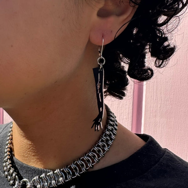 Person wearing a black long glove-shaped earring in front of a pink background