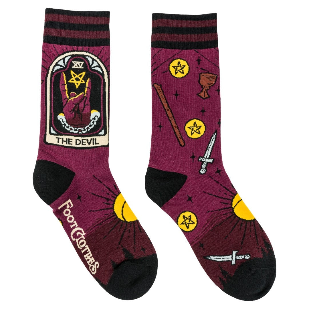 Unisex cotton blend crew socks with striped burgundy and black cuffs and black toes & heels. Each outer ankle has Devil tarot imagery with a hand giving devil fingers alongside a pentagram. Socks have all over pattern of suns, chalices, swords, wands, and pentacles. Shown flat