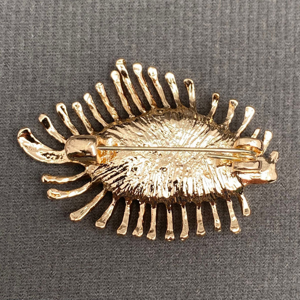 gold metal almond eye-shaped brooch with resin inset eyeball with blue iris and fanned out gold metal eyelashes. Shown from back