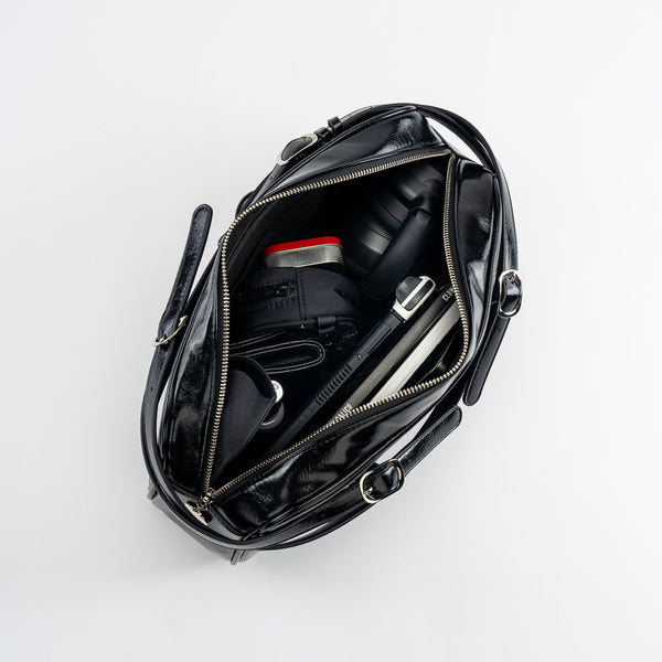 shiny black textured faux leather bowler bag with adjustable shoulder straps, sturdy silver metal zip closure, and studded matching faux leather heart-shaped mirror bag charm. Shown open from top
