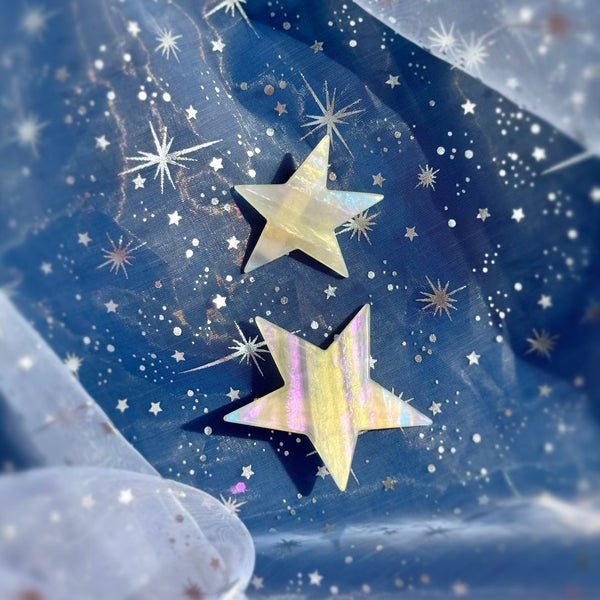 Pair of two different sized asymmetrical star-shaped acetate hair clips with iridescent striped pattern shown on blue sparkly background