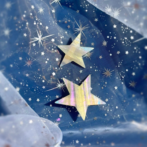 Pair of two different sized asymmetrical star-shaped acetate hair clips with iridescent striped pattern shown on blue sparkly background