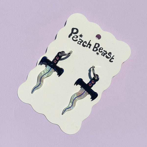 pair of small stainless steel hoop earrings with small acetate dagger charms with wavy iridescent blades and marbled blue and white handles with a row of three rhinestones in each. Shown on backing card