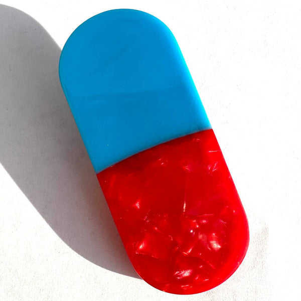 bioacetate hair clip in the shape of a solid light blue and marbled red pill capsule. Shown from front on white background