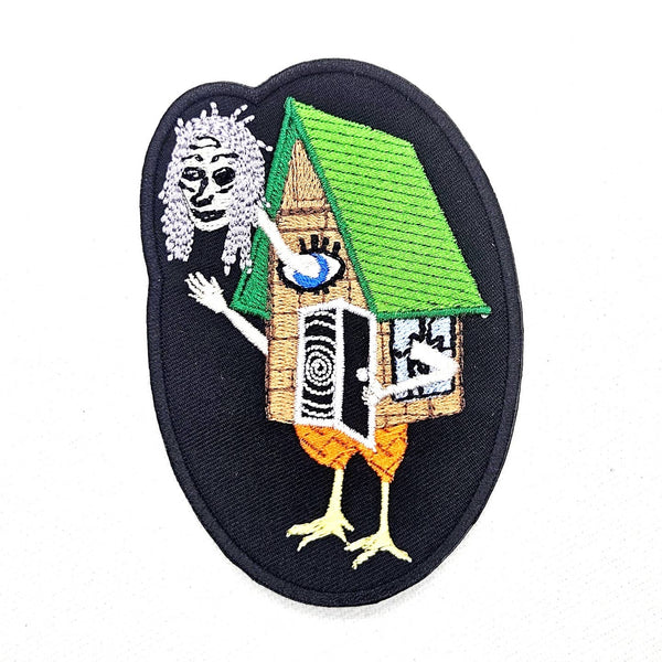 oval shaped twill embroidered patch with image of Baba Yaga and her house on chicken legs with spiral door and large eye. Shown flat