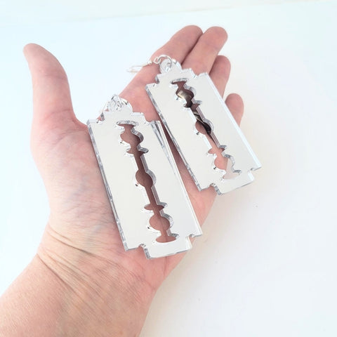 oversized silver mirrored laser cut acrylic razor blade shaped dangle earrings. Shown held in a hand to illustrate size