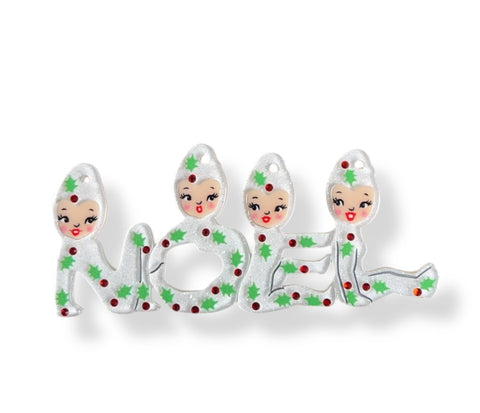 Layered acrylic resin brooch in the shape of four elves wearing white glittery suits decorated with green holly leaves and red jewels spelling out the word “NOEL” with their bodies