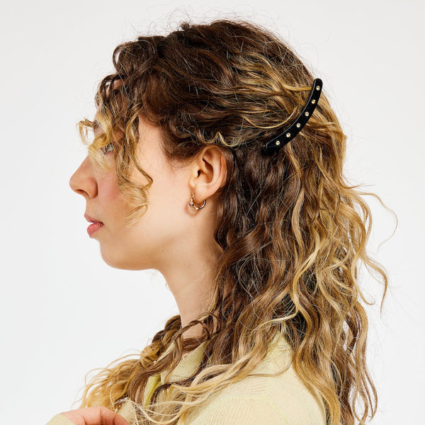 black acetate curved hair clip with flat top decorated with row of 6 clear rhinestones and alligator clip backing. Shown in model's hair