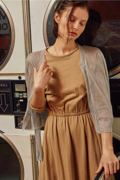 a model wearing an open front cropped cardigan with long sleeves in a semi-translucent silver lurex knit. It has ribbed cuffs and hems. Shown from the front