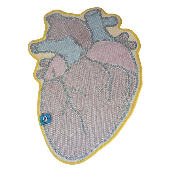 A colorful tufted rug shaped like a stylized anatomical heart, featuring red, pink, and blue sections outlined in black with a brifght yellow border, shown from the back on a plain white background. Displays branded tag and rubber non-slip backing