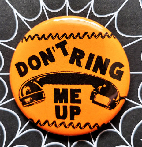 1.25” round pinback button “Don’t Ring Me Up” with illustration of rotary phone and telephone cord in black on an orange background 