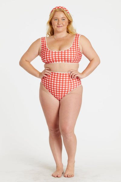 model wearing red and white gingham print reversible bikini. Top has scoop neckline and white rickrack style trim. Shown from front with gingham side worn