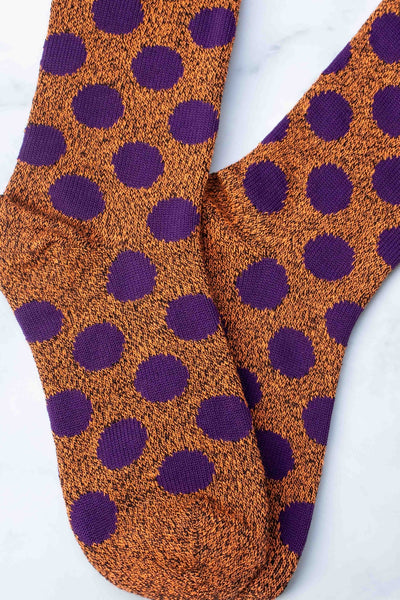 rusty orange heathered socks with eggplant purple polka dots on a marble background shown in close up