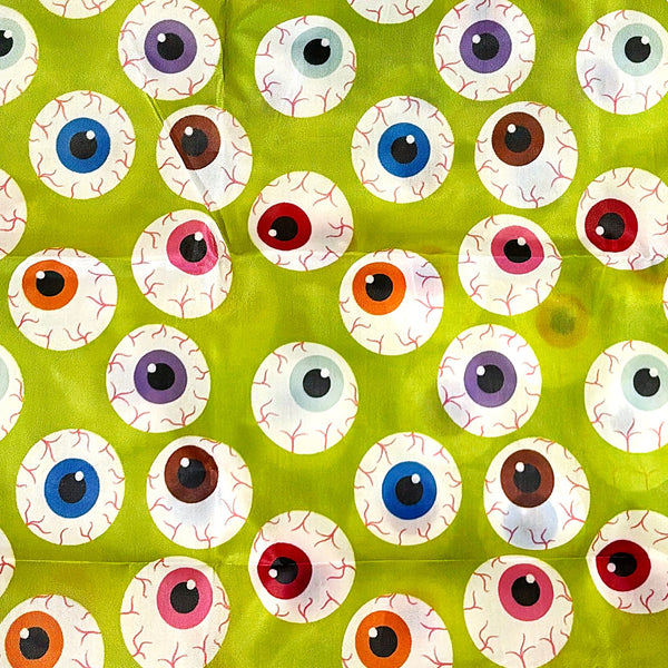 A lime green reusable nylon tote bag with an all-over pattern of large cartoonish eyeballs in various colors shown in close up shot of pattern
