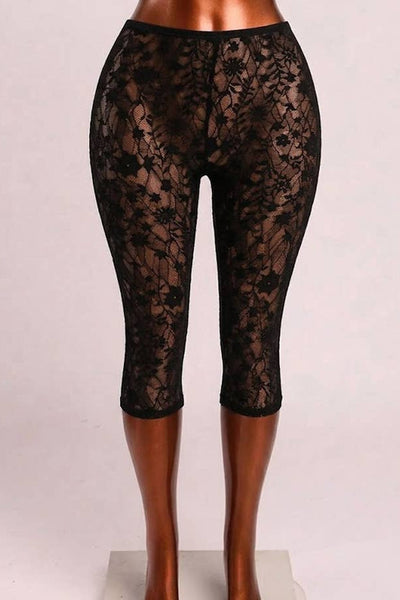 Black floral patterned lace high-waist capri length leggings displayed on a mannequin leg form against a light gray studio background.Shown from front