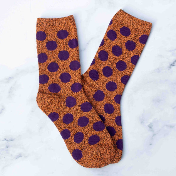 rusty orange heathered socks with eggplant purple polka dots on a marble background