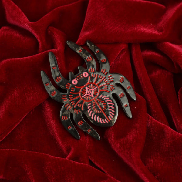 black marbled acetate hair clip in the shape of a spider with red and pink line detail and pink eyes. Shown on red velvet background