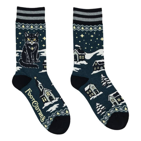 Unisex crew socks in dark teal with black and grey striped cuffs and black toes & heels. All over pattern of black cat scowling with Fair Isle snowflake and tree pattern & snowy trees and houses. Shown flat