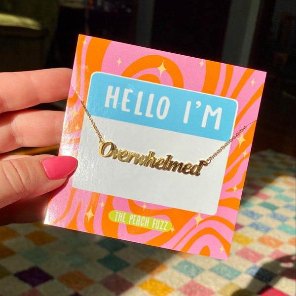 Gold covered stainless steel link chain necklace with 'Overwhelmed' nameplate pendant on 'Hello I'm' backing card