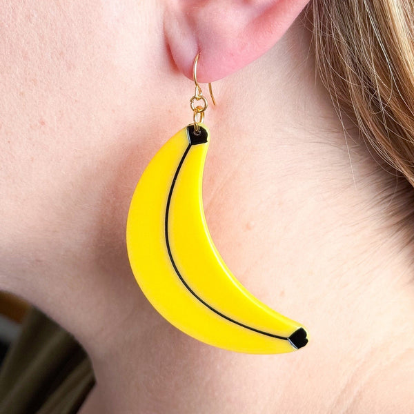 cellulose acetate dangle earrings in the shape of a pair of yellow bananas with black detail. Shown on model