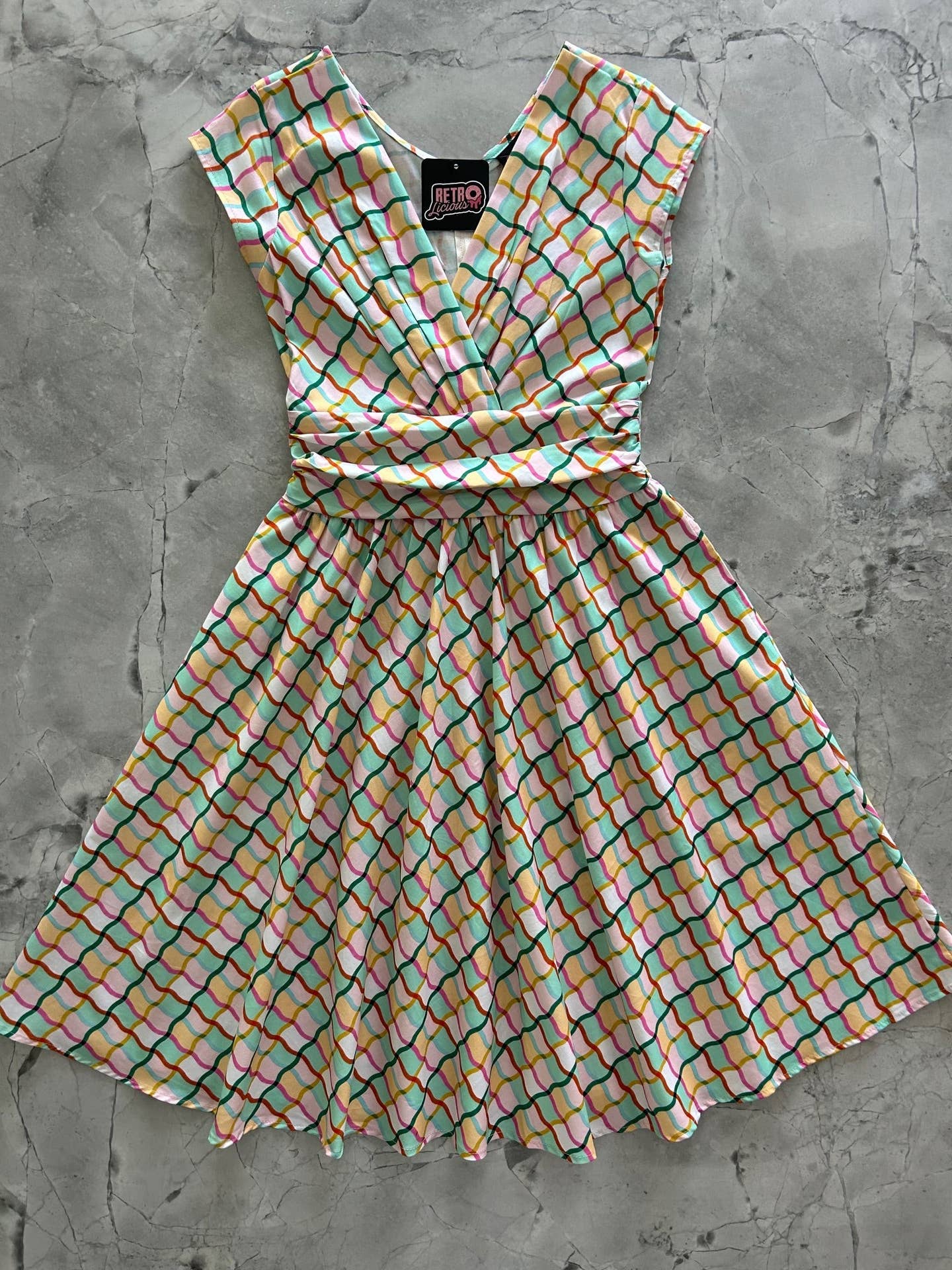 dress with surplice style neckline, cap sleeves, wide cummerbund style waistband, and full below the knee skirt with pockets. All-over print of wavy windowpane pattern in overlapping shades of light pink, teal, red, mustard, and minty green. Shown laid flat