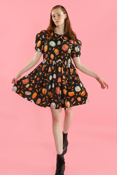 model wearing a babydoll style dress with a black background photorealistic collage pattern of doll heads and arms. It has a ruffled Peter Pan style collar, puffed short sleeves, and a gathered double tiered above the knee skirt. Shown from the front 