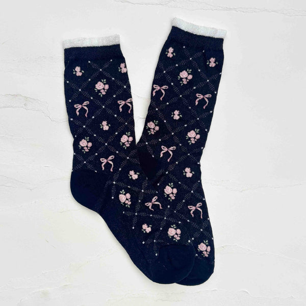 A pair of black crew socks with white trimmed cuffs and a pink rose and bow pattern on an openwork diamond pattern background