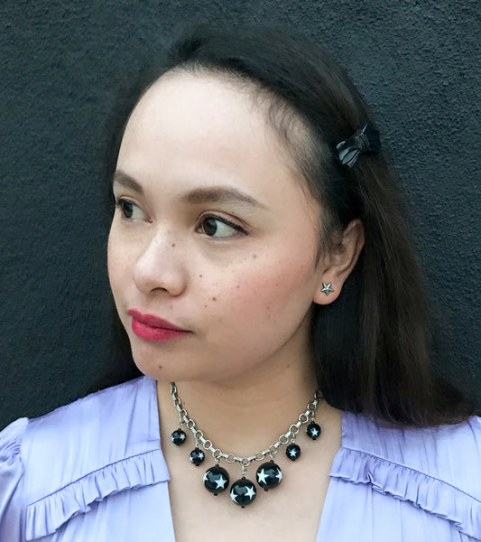 model wearing link necklace with 7 varying sizes of round black beads decorated with white stars 