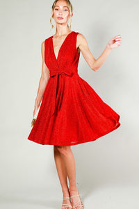 bright red lurex sleeveless dress featuring pleated surplice v-neck bodice, banded waist with removable matching sash belt, and a swing-y full circle just-above-the-knee length skirt. shown on a model.
