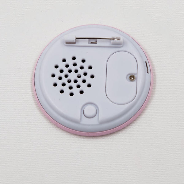 A round pink button badge featuring a black-and-white illustrated portrait of John Waters wearing sunglasses, with red text reading 'GET AWAY FROM ME!' and black text reading 'JOHN WATERS'. Shown from back to display speaker, button, and battery slot