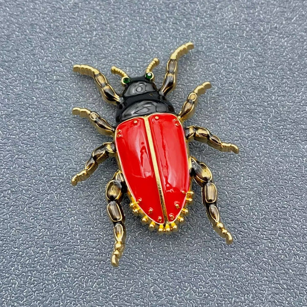 gold metal enameled beetle brooch with bright red enameled abdomen, black head, gold legs, and small green jeweled eyes. Shown flat