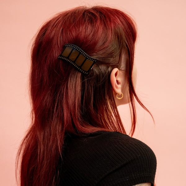 Translucent tawny brown acetate alligator style hair clip in the shape of a film strip shown in model’s updo