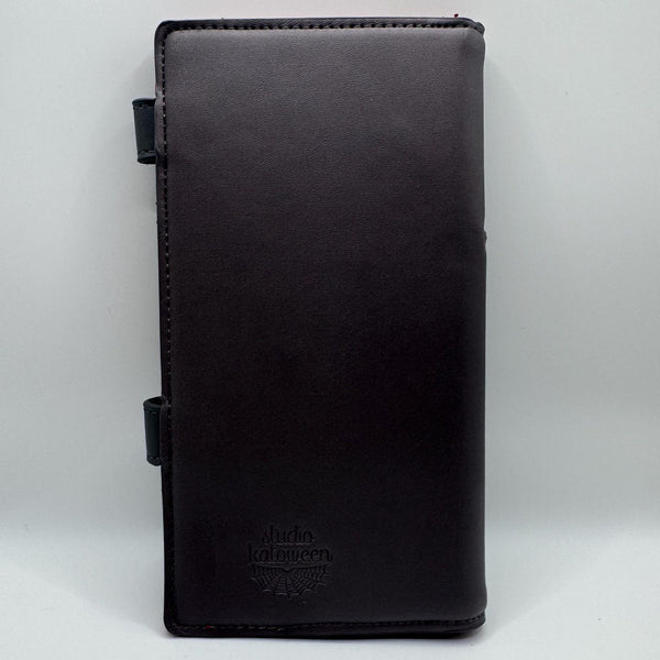 black faux leather wallet in the shape of a casket with two separate silver metal snap closures to replicate the headpanel and footpanel. Shown closed from back