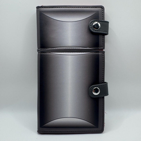 black faux leather wallet in the shape of a casket with two separate silver metal snap closures to replicate the headpanel and footpanel. Shown closed from front