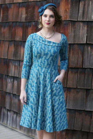 stretch cotton knit 3/4 sleeved fit and flare dress in a teal and cream rosemary sprig pattern and features an asymmetrical rolled neckline, and finishes with a swingy knee length skirt