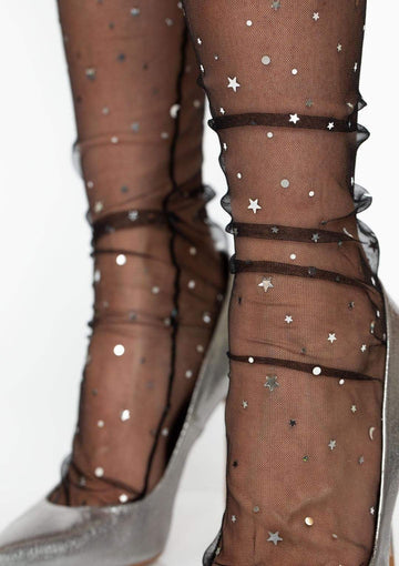 Model wearing black mesh crew socks with silver moon, star, and round silver confetti embellishments. Shown from side in close up 