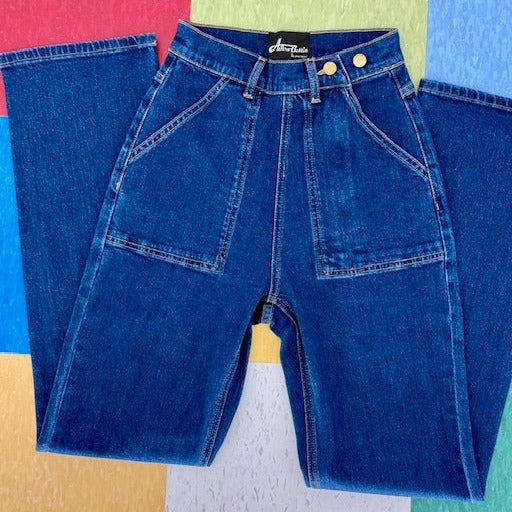 dark wash 1950's reproduction stretch denim jeans with double button at waist, deep front hip pockets, and zip closure at left side hip. Shown flat on colored linoleum tile background 