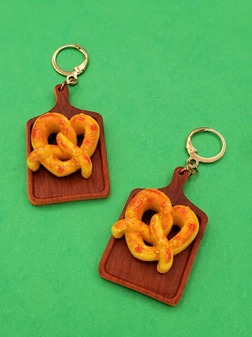 Acrylic dangle earrings with hinge back ear wires in the shape of wooden cutting boards with a large golden pretzel on each