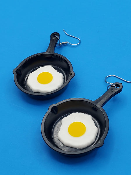 pair of dangle earrings with charms in the shape of cast iron frying pans with sunny side up eggs in each pan