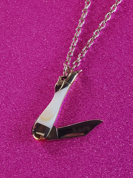 An 18” silver metal chain link necklace with a mini pocket knife charm in the shape of a white marbled enameled leg wearing a silver high heel shoe. showing close up of pendant partially opened with knife visible
