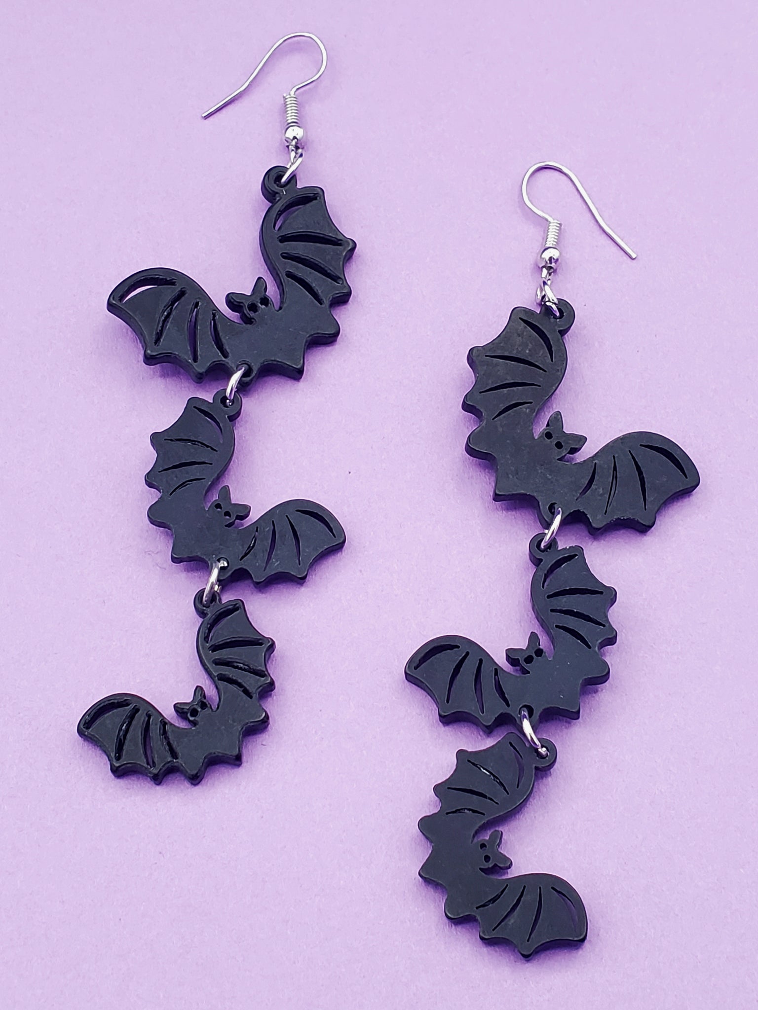 pair of dangle earrings, each comprised of three graduated size matte black laser-cut acrylic bats linked together in a line